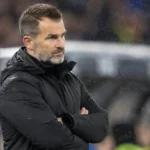 Een niet-spelende Club Brugge-vertegenwoordiger in een zwarte jas langs de zijlijn.