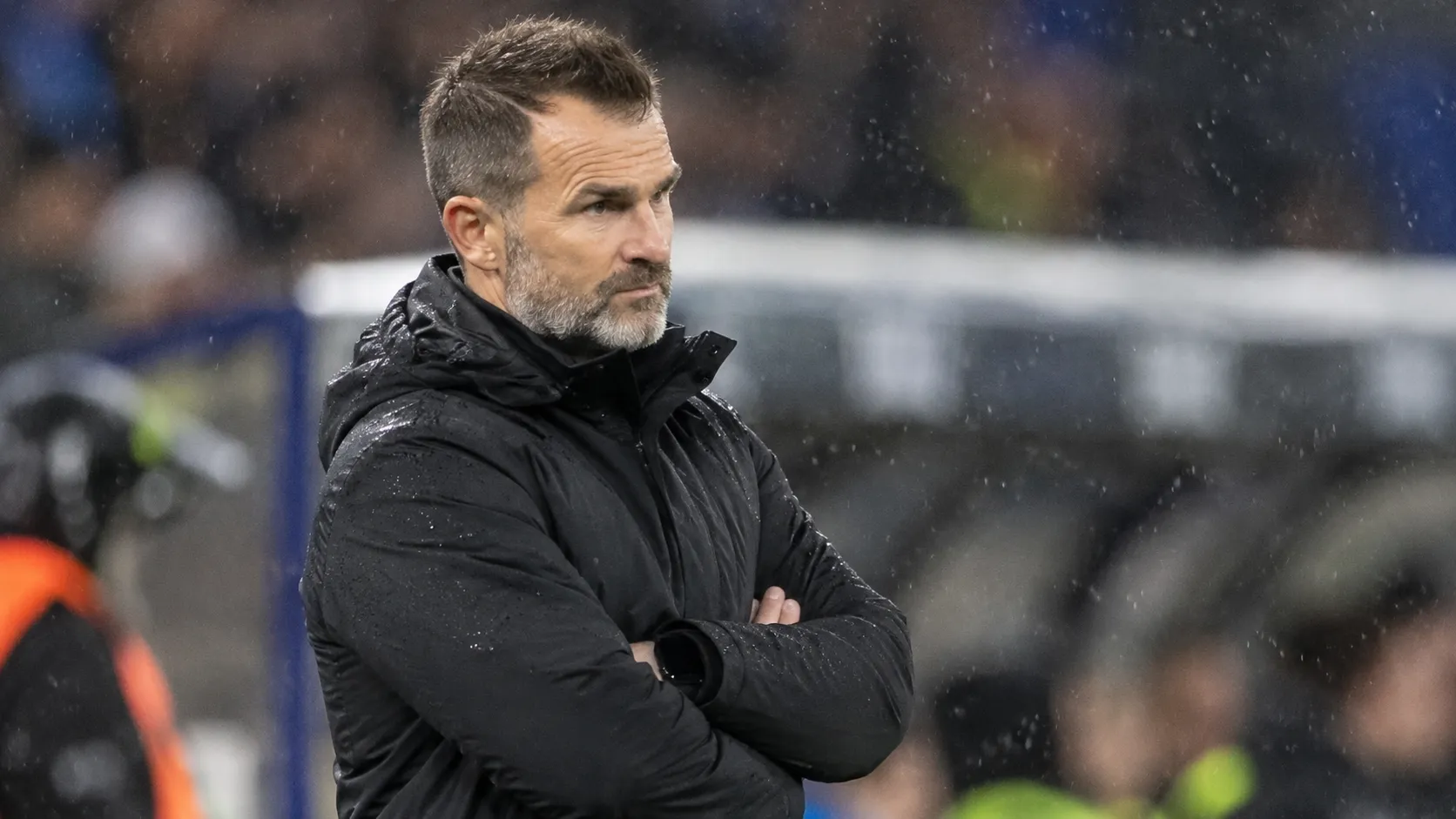 Een niet-spelende Club Brugge-vertegenwoordiger in een zwarte jas langs de zijlijn.