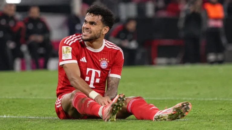 Luis Díaz zit op het gras in het Bayern München-tenue en kijkt richting de dug-out.
