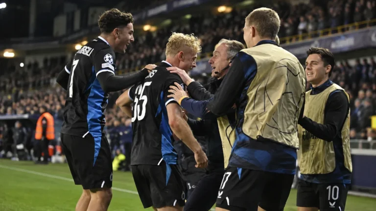 Een groep voetballers viert langs de zijlijn in zwart-blauwe wedstrijdkleding.