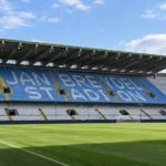 Lege hoofdtribune van het Jan Breydelstadion met blauw-witte zitjes en het speelveld.