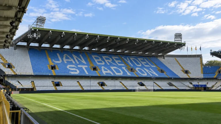 Lege hoofdtribune van het Jan Breydelstadion met blauw-witte zitjes en het speelveld.