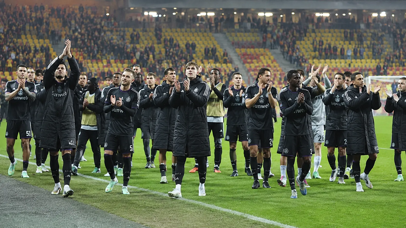 Een groep Anderlecht-spelers applaudisseert na afloop op het veld van een Europees stadion.