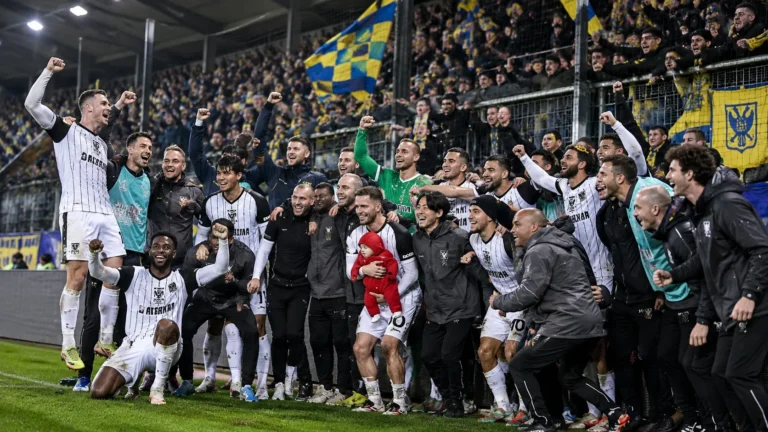 Spelers en staf vieren samen een Europese uitzege aan de rand van het veld.