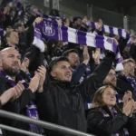 Een groep Anderlecht-supporters viert samen in de tribune met paarse en witte sjaals.