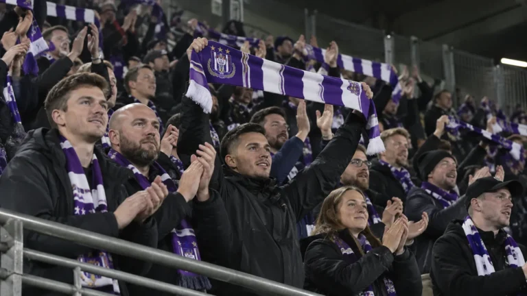Een groep Anderlecht-supporters viert samen in de tribune met paarse en witte sjaals.