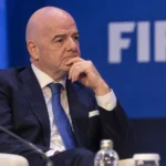 Gianni Infantino luistert in een congreszaal naar een toespraak voor een FIFA-embleem.