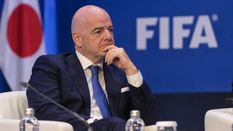 Gianni Infantino luistert in een congreszaal naar een toespraak voor een FIFA-embleem.