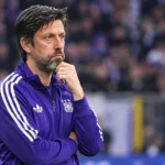Een Anderlecht-trainer in een paarse trainingsjas langs de zijlijn.