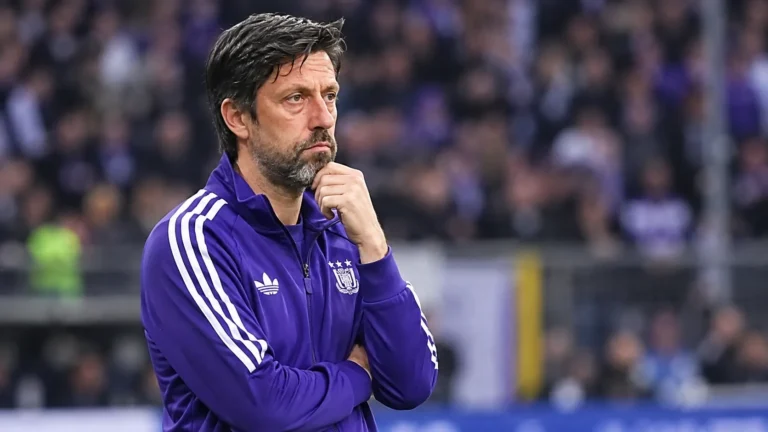 Een Anderlecht-trainer in een paarse trainingsjas langs de zijlijn.