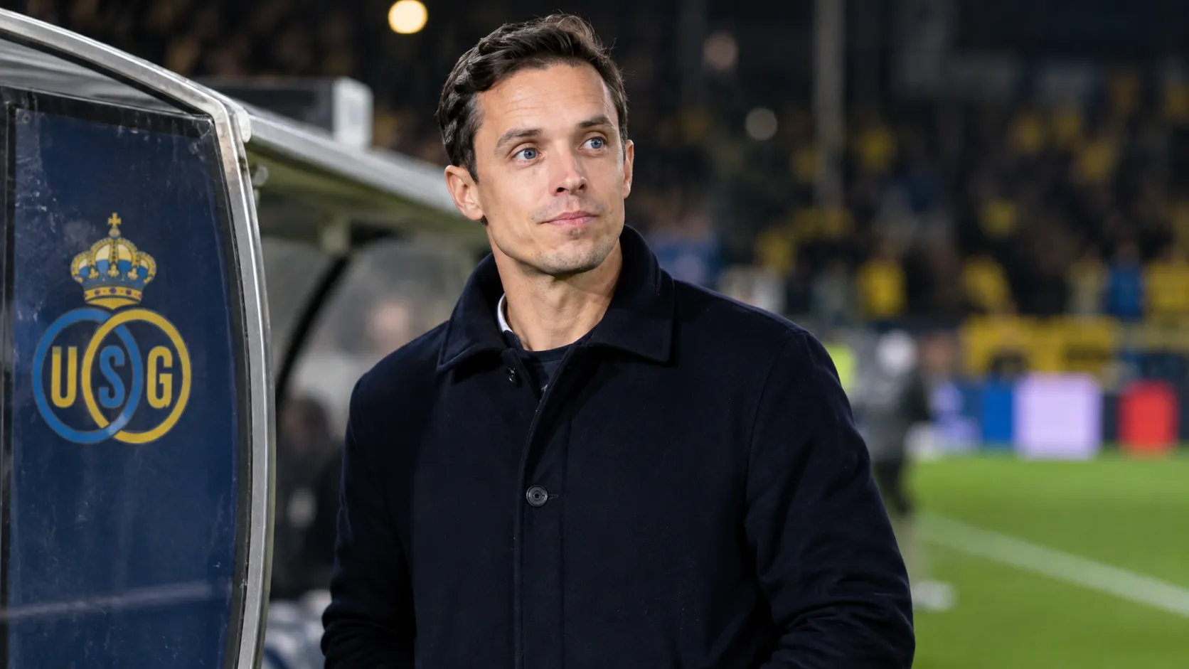 David Hubert in donkere jas aan de zijlijn bij een technische zone van Union Saint-Gilloise.