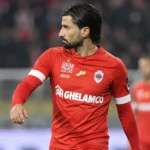 Een speler van Royal Antwerp FC in rood tenue tijdens een rustig moment op het veld.