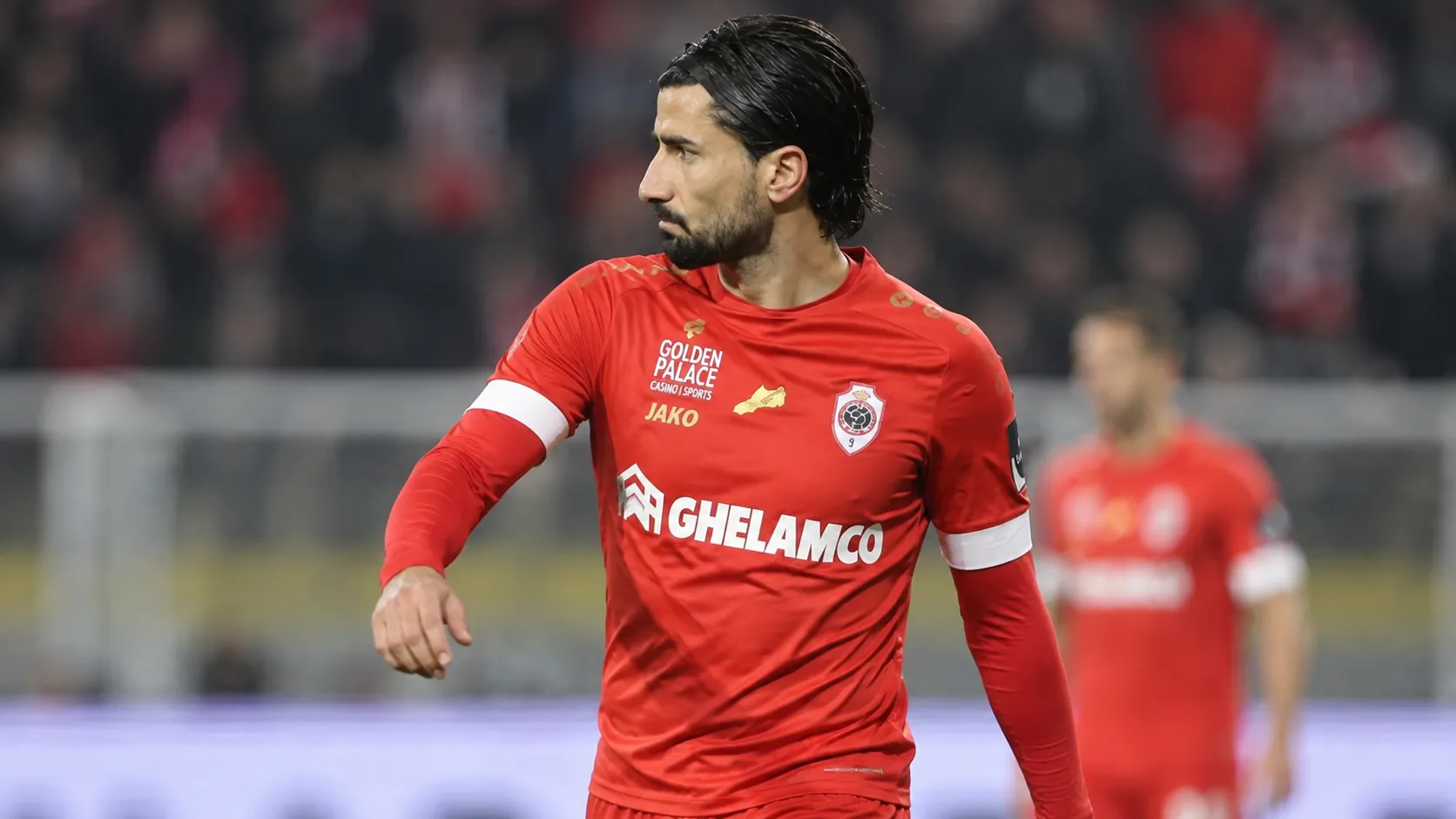 Een speler van Royal Antwerp FC in rood tenue tijdens een rustig moment op het veld.