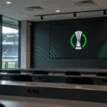 Lege mediazone in een Conference League-stadion met een digitaal competitiescherm.
