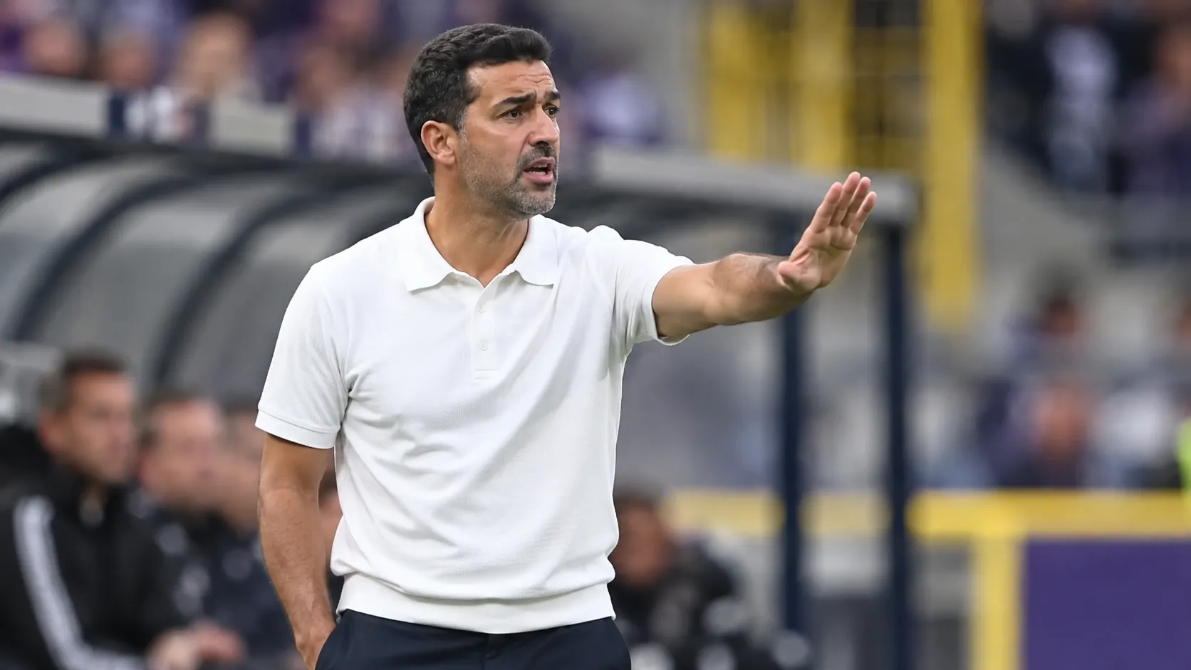 Mo Messoudi geeft instructies langs de zijlijn in een wit poloshirt.