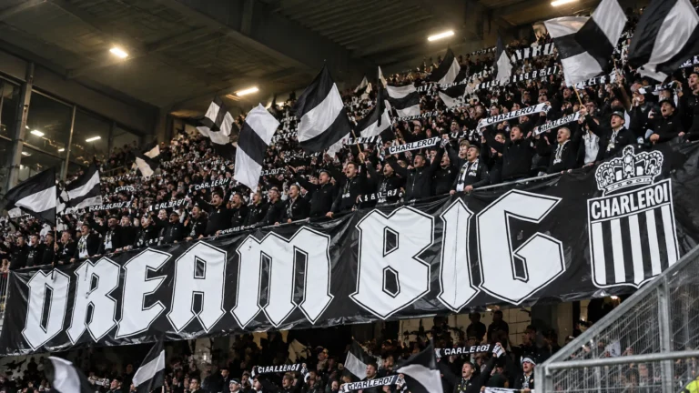Een volle tribune met zwart-witte supporters die vlaggen omhooghouden.