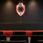 Een leeg persconferentiepodium van Royal Antwerp FC met een clubembleem op de achterwand.