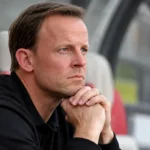 Een Standard-coach zit geconcentreerd in de technische zone langs het veld.