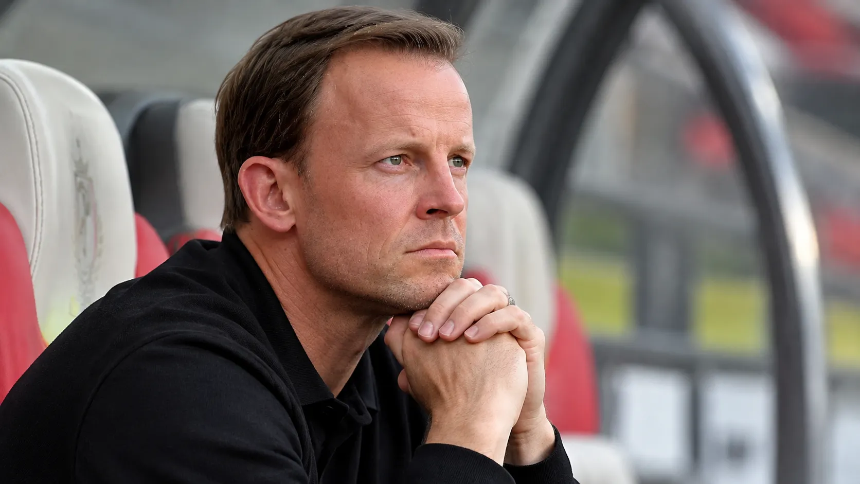 Een Standard-coach zit geconcentreerd in de technische zone langs het veld.