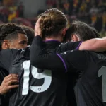 Spelers in donkere shirts omhelzen elkaar na een voetbalwedstrijd.