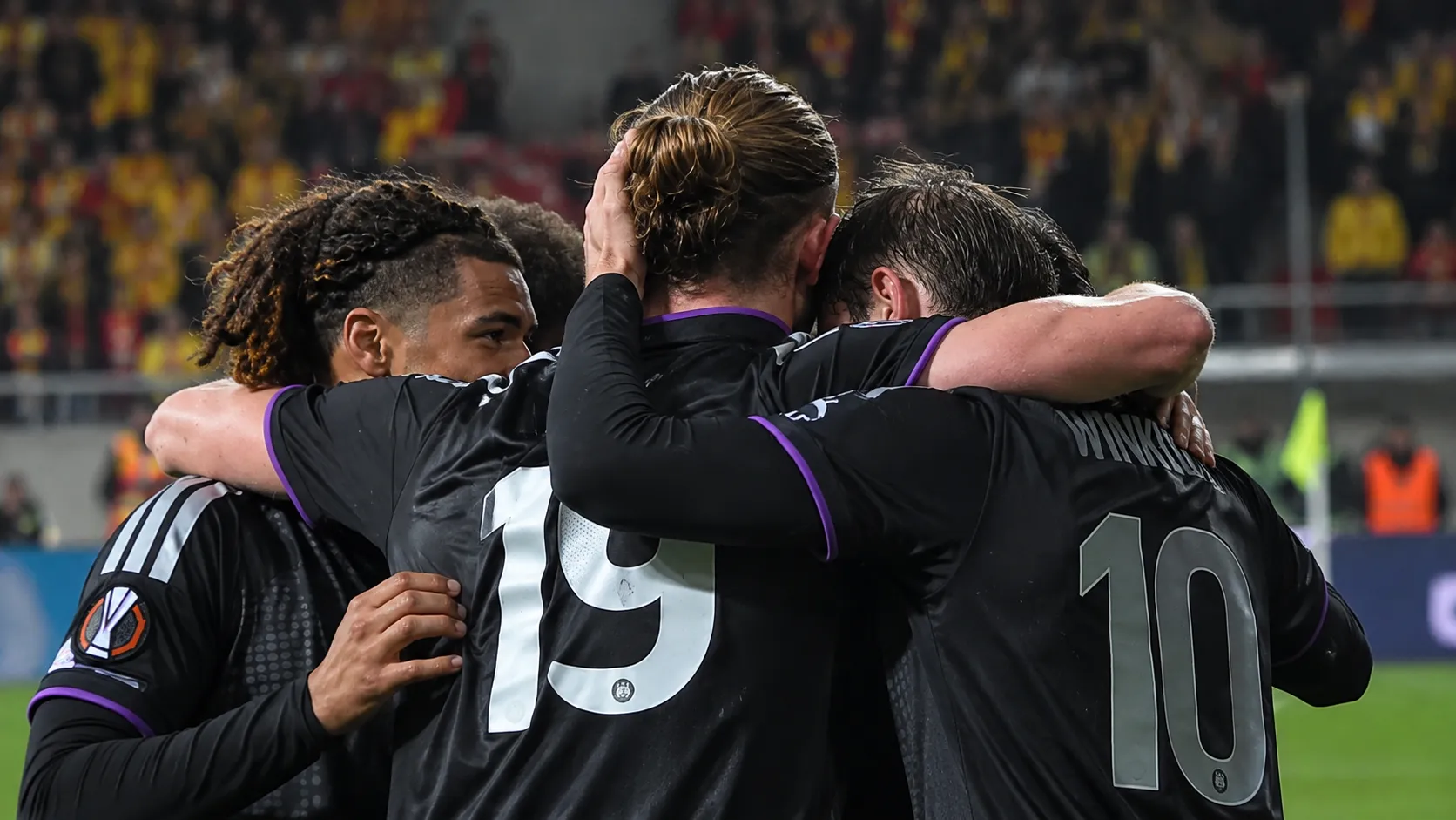 Spelers in donkere shirts omhelzen elkaar na een voetbalwedstrijd.