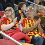 Supporters in rood-geel op de tribune van een Belgisch voetbalstadion.