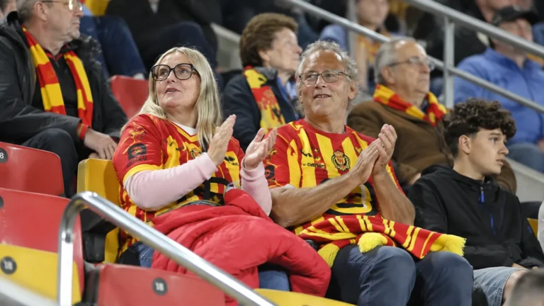 Supporters in rood-geel op de tribune van een Belgisch voetbalstadion.
