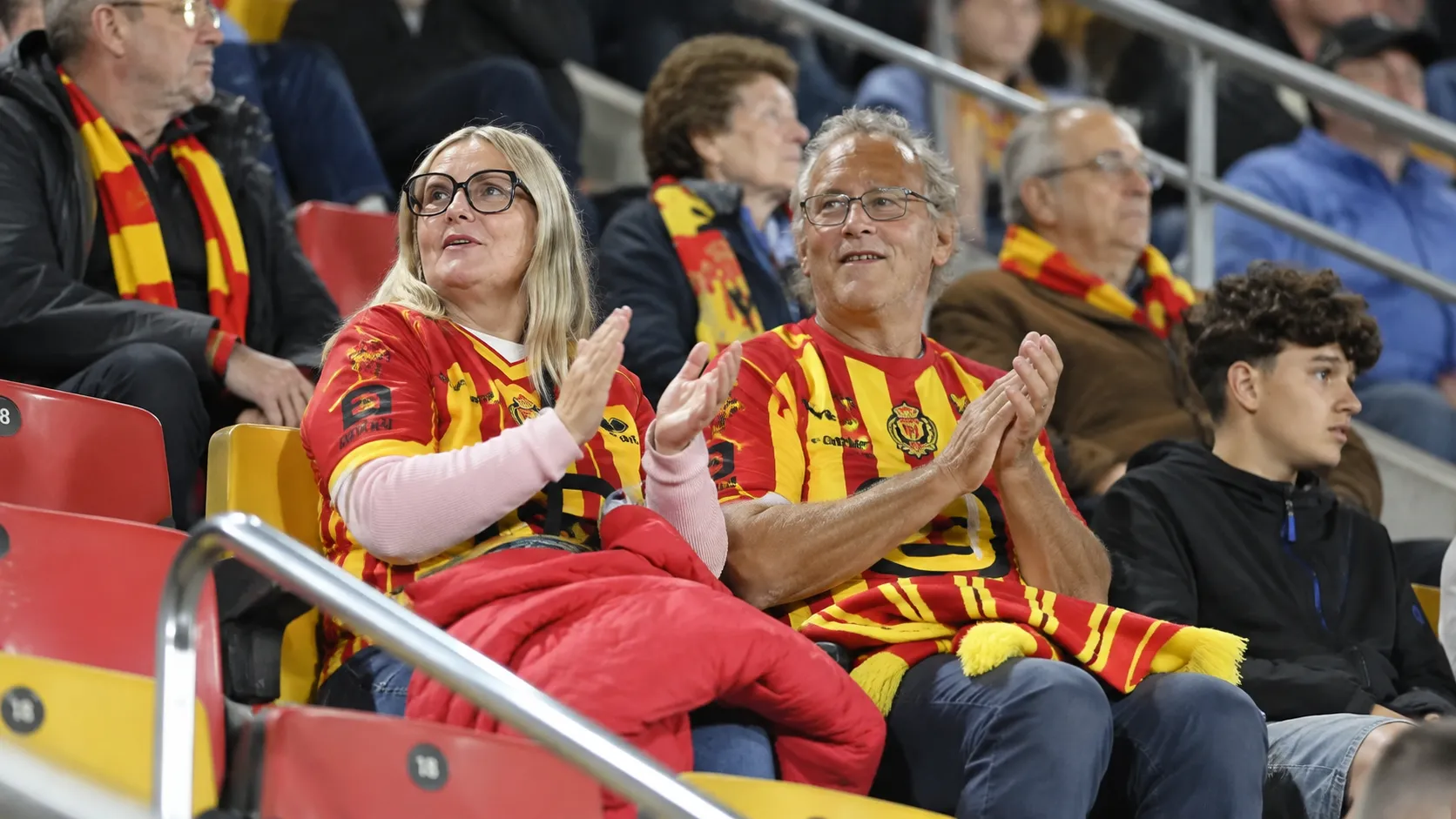 Supporters in rood-geel op de tribune van een Belgisch voetbalstadion.