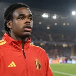 Nathan Ngoy in een rode jas van de Belgische nationale ploeg langs het veld na een interland.
