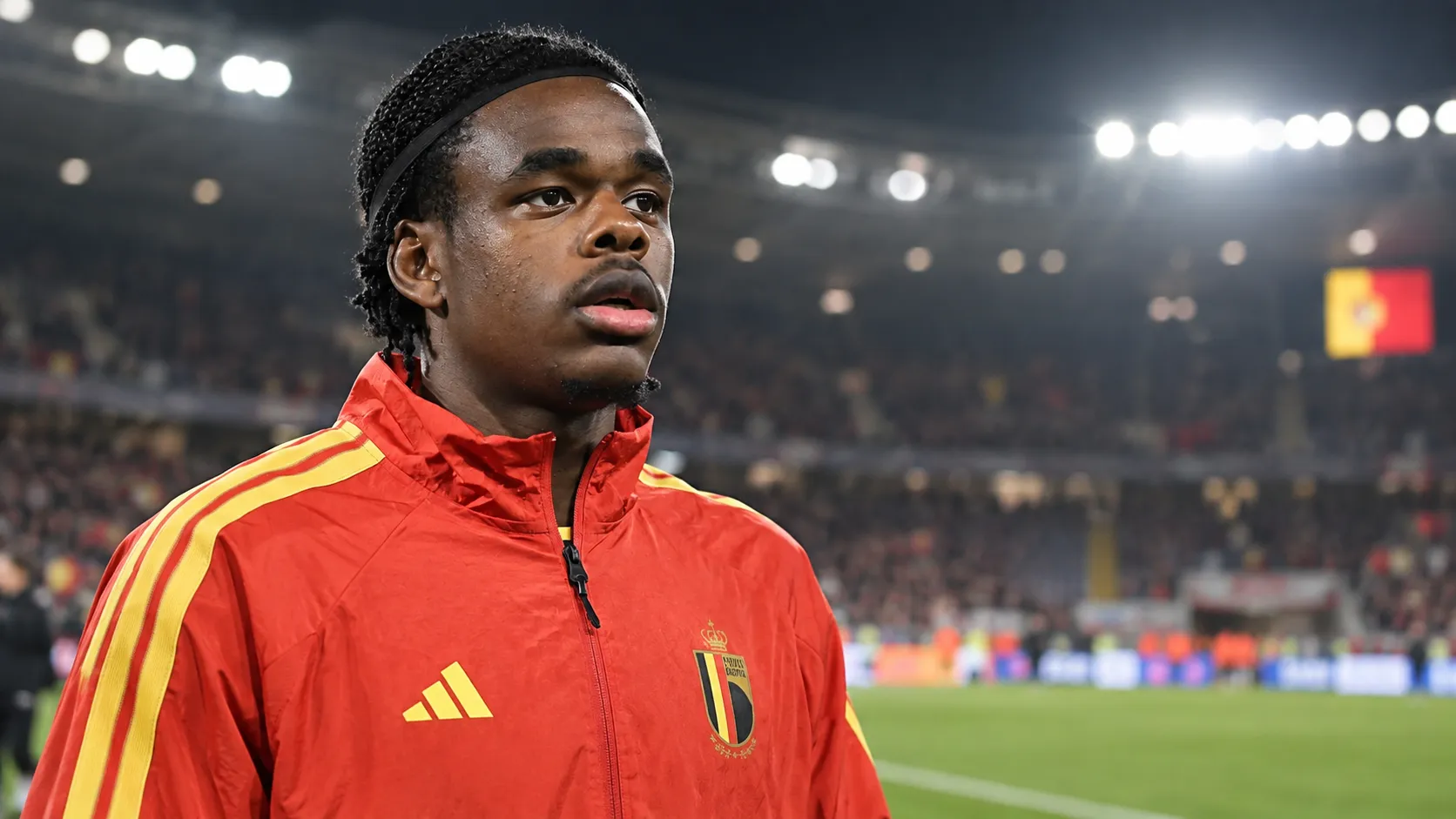 Nathan Ngoy in een rode jas van de Belgische nationale ploeg langs het veld na een interland.