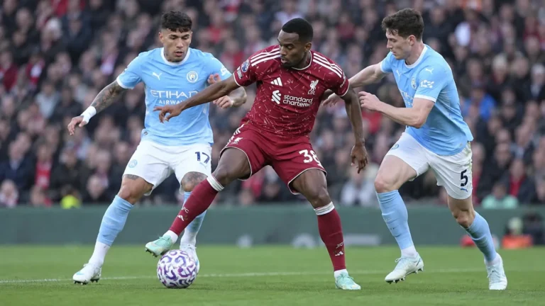 Een Liverpool-speler in donkerrood strijdt om de bal met twee tegenstanders in lichtblauw.