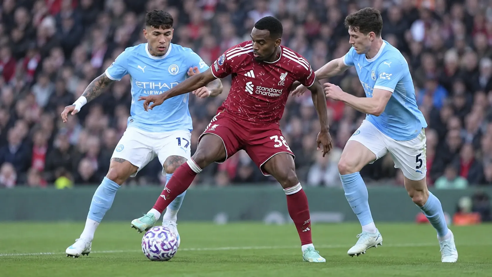 Een Liverpool-speler in donkerrood strijdt om de bal met twee tegenstanders in lichtblauw.