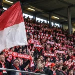 Een groep KV Kortrijk-supporters met rood-witte sjaals op een overdekte tribune.