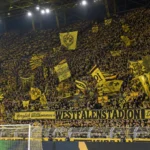 Een volle tribune met Borussia Dortmund-supporters die gele vlaggen zwaaien.