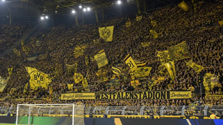 Een volle tribune met Borussia Dortmund-supporters die gele vlaggen zwaaien.