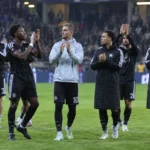 Anderlecht-spelers in donkere clubkleding applaudisseren na een Europese uitwedstrijd.