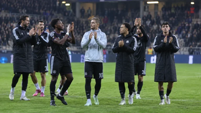 Anderlecht-spelers in donkere clubkleding applaudisseren na een Europese uitwedstrijd.