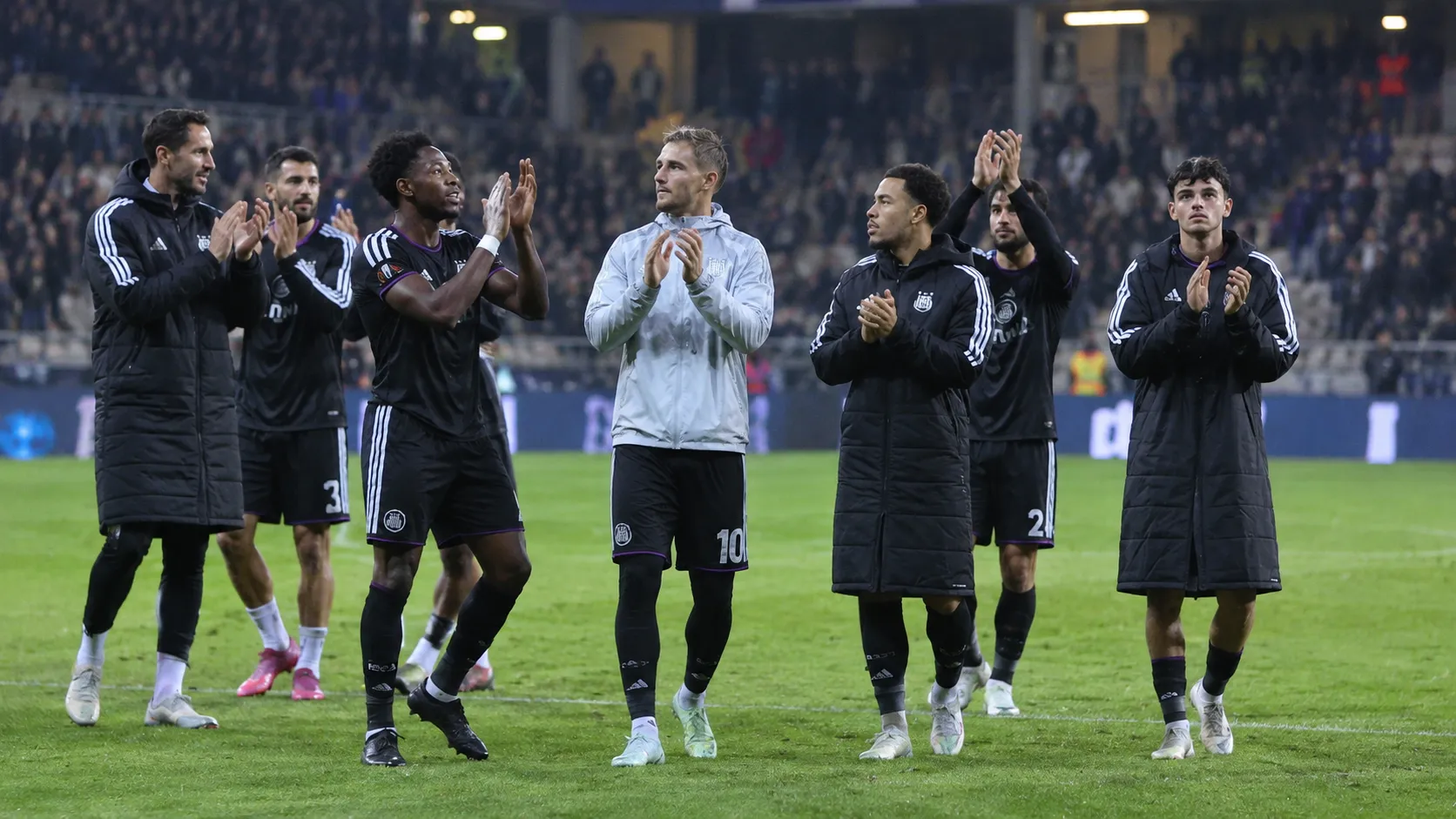 Anderlecht-spelers in donkere clubkleding applaudisseren na een Europese uitwedstrijd.