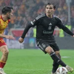 Twee voetballers tijdens een regenachtige wedstrijd in een Europees stadion.
