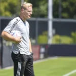 Olivier Deschacht in grijze trainingskleding aan de rand van een voetbalveld.