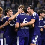 Een groep Anderlecht-spelers viert samen op het veld in paarse wedstrijdtenues.