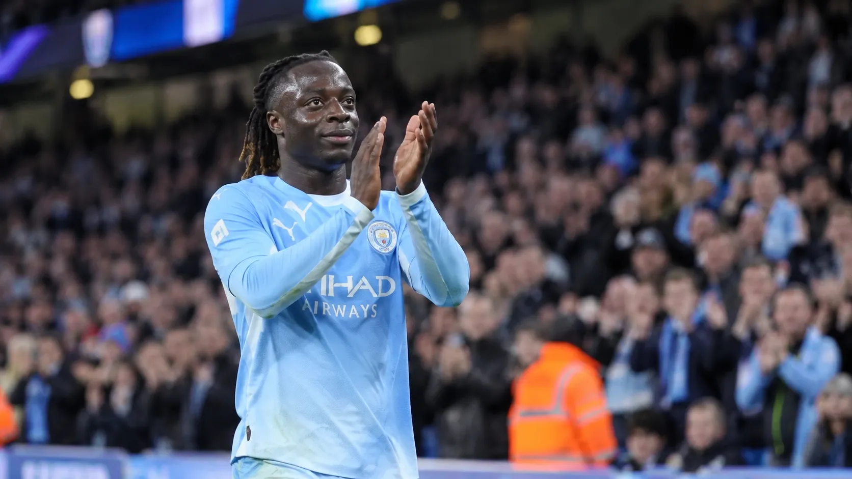 Jérémy Doku applaudisseert in zijn lichtblauwe Manchester City-tenue richting de tribunes.