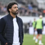 Marvin Compper kijkt vanaf de zijlijn naar de warming-up op een voetbalveld.