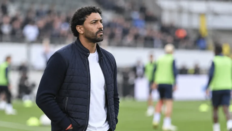 Marvin Compper kijkt vanaf de zijlijn naar de warming-up op een voetbalveld.
