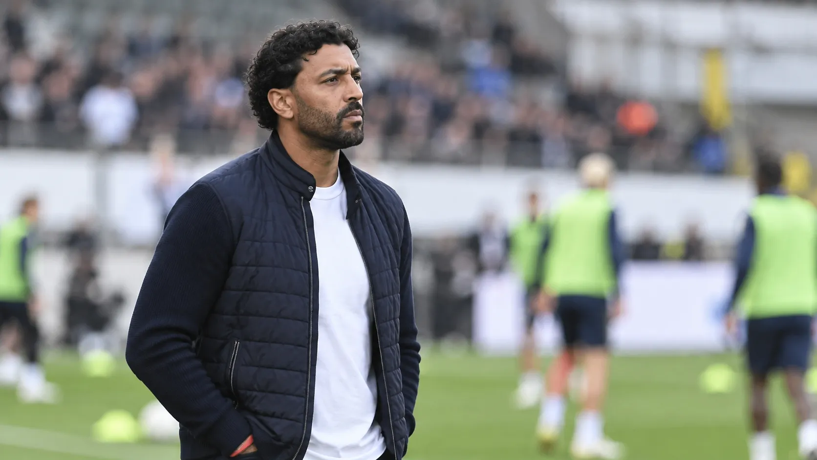 Marvin Compper kijkt vanaf de zijlijn naar de warming-up op een voetbalveld.
