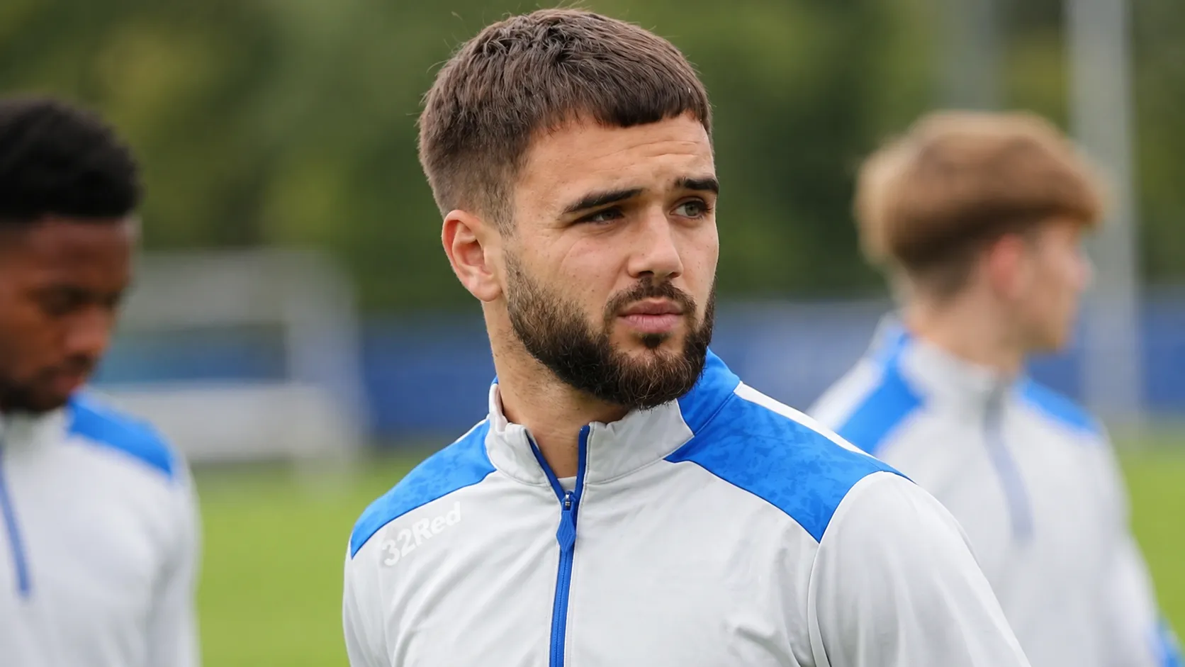 Nicolas Raskin in een wit-blauw trainingsvest op een grasveld.