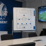 Lege videoanalyseruimte van KAA Gent met een magnetisch tactiekbord en clubembleem aan de wand.
