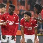 Een groep spelers van Standard viert samen in rode shirts tijdens een regenachtige wedstrijd.