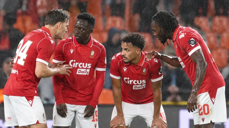Een groep spelers van Standard viert samen in rode shirts tijdens een regenachtige wedstrijd.