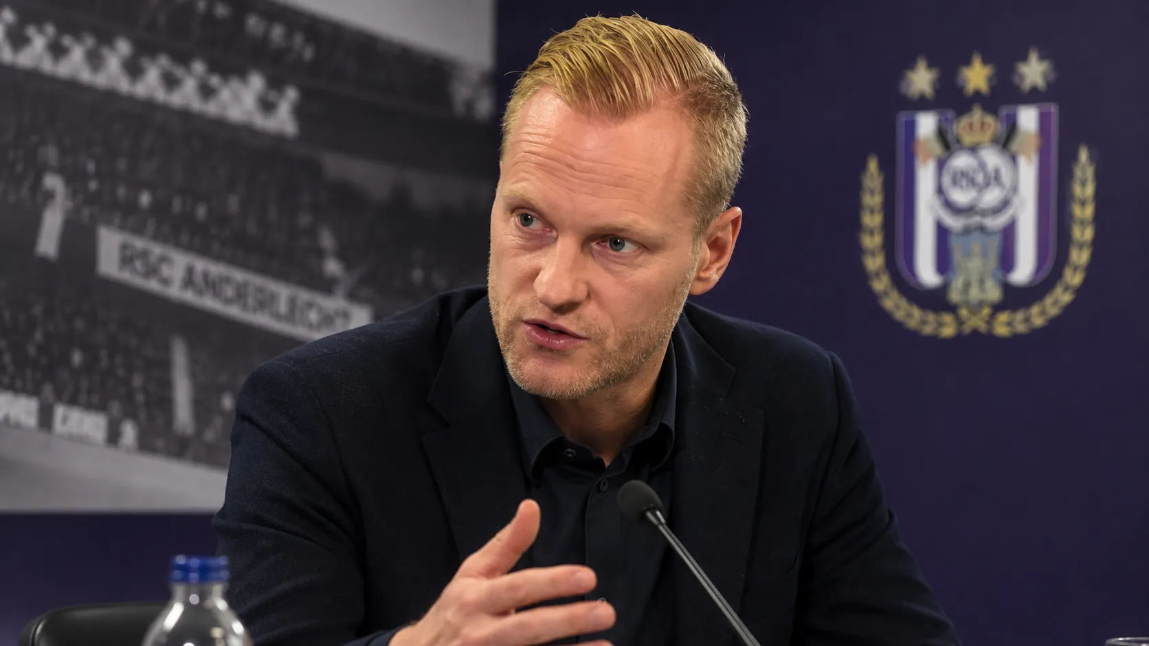 Olivier Deschacht spreekt in een stadionperszone met een discreet Anderlecht-embleem op de wand.